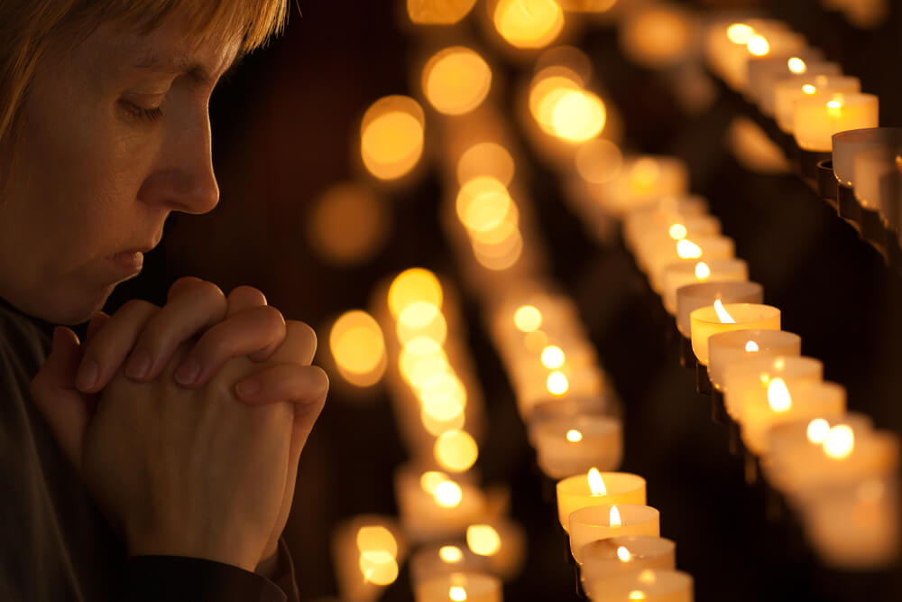 Woman Praying in Front of Catholic Burning Candles